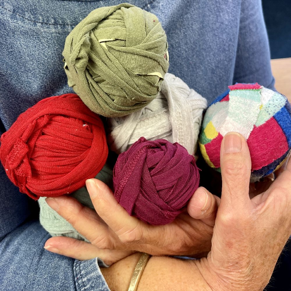 Close up of hands holding five balls of different coloured yarns made from old clothes