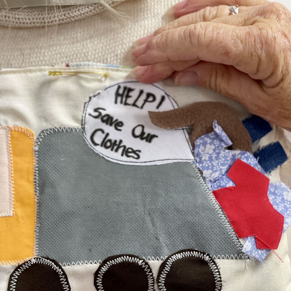 Close up photo of an appliques mural of a rubbish truck with clothes in the back and a speech bubble with the words, 'Help! Save Our Clothes'