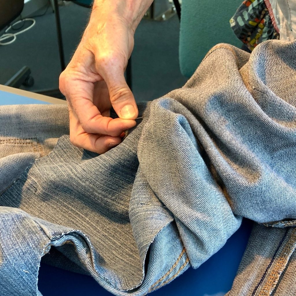 Close up photo of a pair of trousers being repaired by hand with a needle and thread